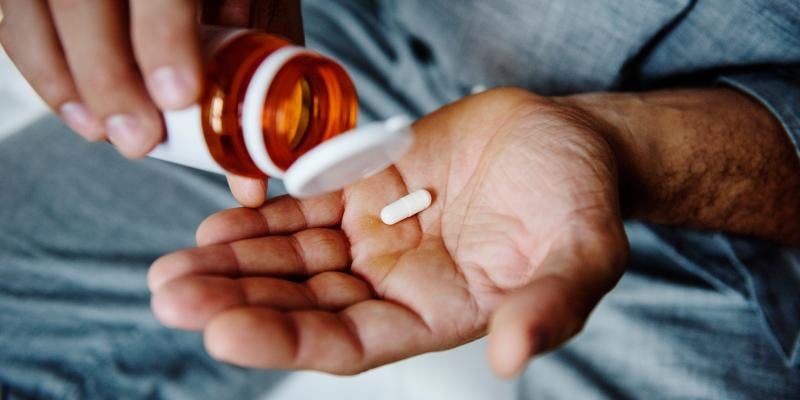 A man placing a single tablet into his palm from a small bottle of medication