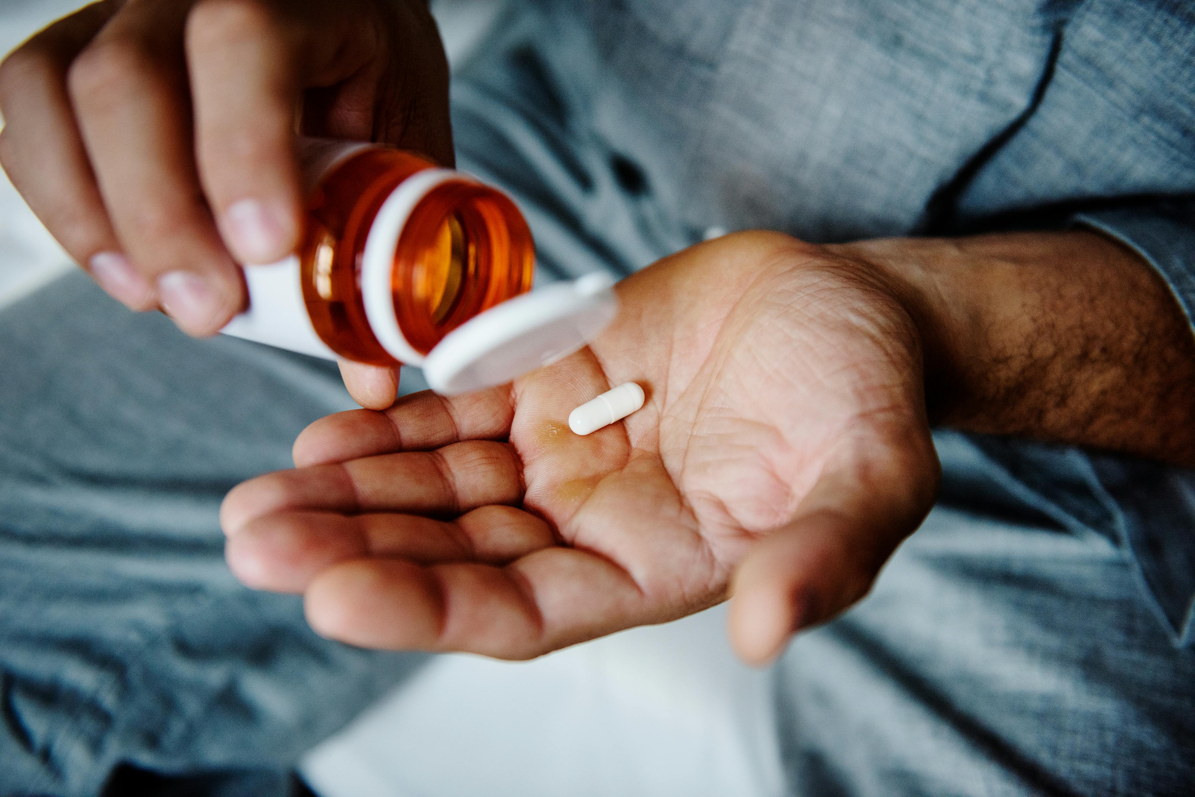 A man placing a single tablet into his palm from a small bottle of medication