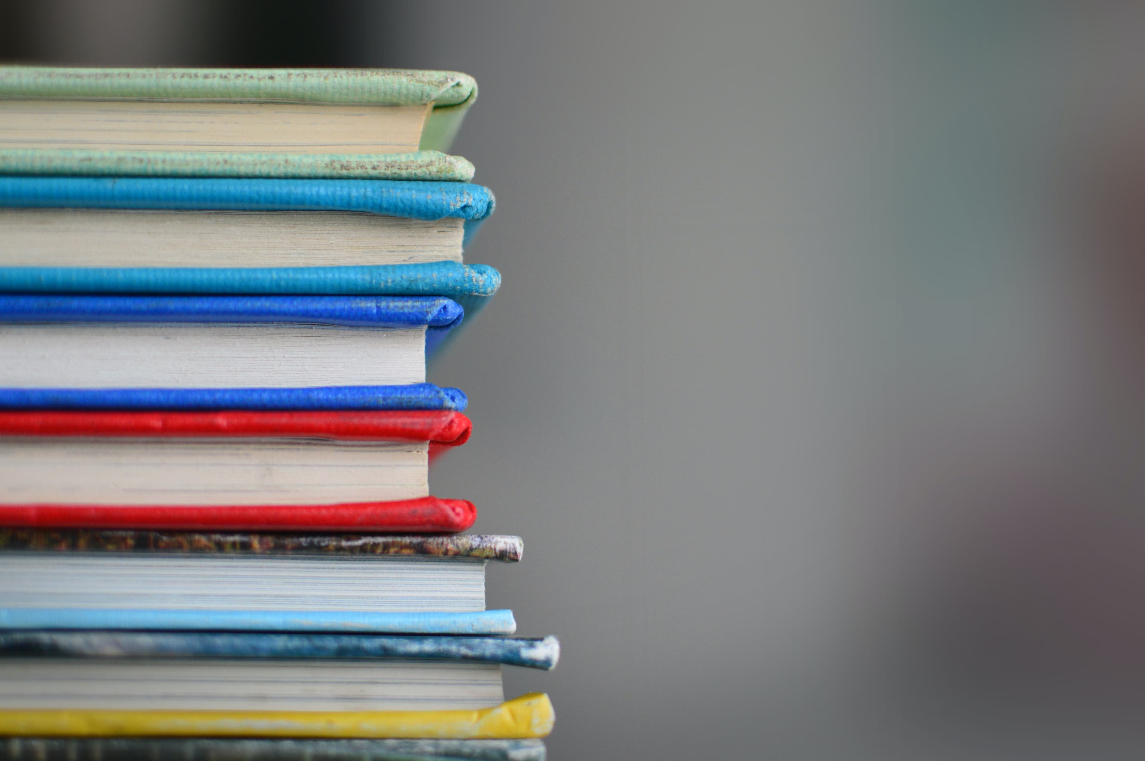 A close-up of six books with colored covers lying on their sides in a stack.
